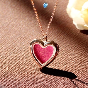 Close-up of rose gold heart locket necklace with pink glitter inlay on brown fabric
