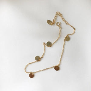 Close-up of gold S925 sterling silver anklet featuring minimalist round disc charms