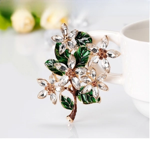 Detail of flower brooch with green enamel leaves and crystals on white ceramic cup