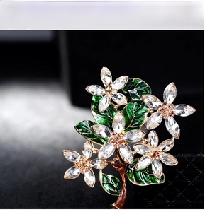 Macro detail of enamel flower brooch with green leaves and clear crystal petals