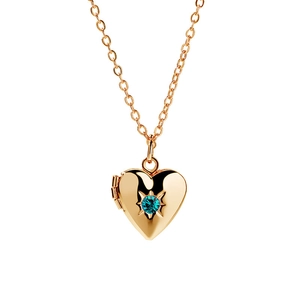 Dettaglio di un medaglione a cuore dorato con una pietra preziosa blu incastonata