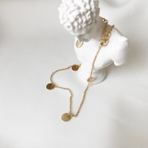 Detail view of a gold circular disc anklet elegantly draped on a white plaster bust