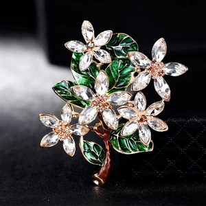 Vintage floral brooch with green enamel leaves and sparkling crystals on a dark surface