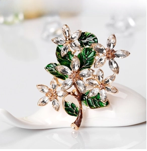 Macro shot of floral brooch with white crystals and green enamel leaf on ceramic