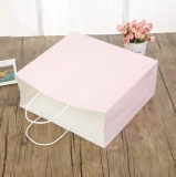 Detailed view of pink paper gift bag with white round handles on a wooden table
