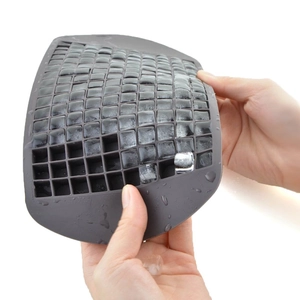 Hands bending flexible grey silicone honeycomb tray to release frozen square ice cubes