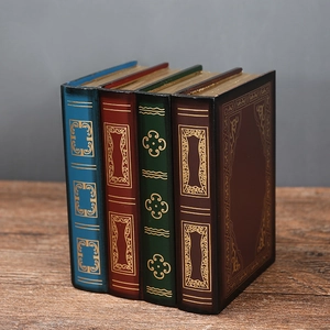 Close-up of four vintage faux book storage boxes with gold patterns on a wooden table