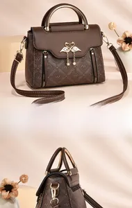 Detail of dark brown leather handbag featuring gold swan clasp and pearl pendant accent