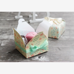 Macro shot of floral paper gift box with mint green ribbon and two macarons inside