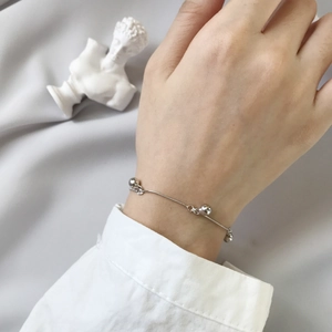 Detail of silver ball pendant bracelet on wrist styled with a white shirt sleeve