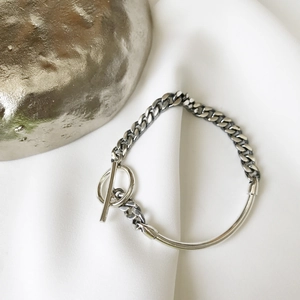 Detail of silver chain bracelet with OT buckle and asymmetric design on white fabric