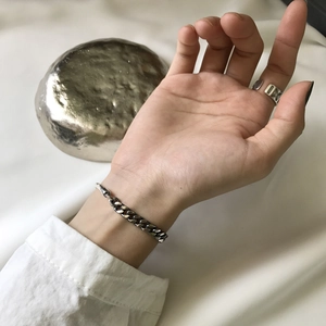 Macro shot of 925 sterling silver chain bracelet and hollow geometric ring on hand