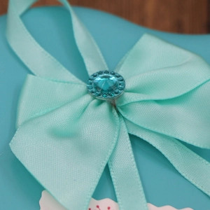 Macro shot of a mint green satin bow with a faceted gemstone on a heart-shaped gift box