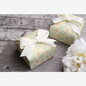Detailed view of two square floral paper gift boxes with white ribbon bows on wood