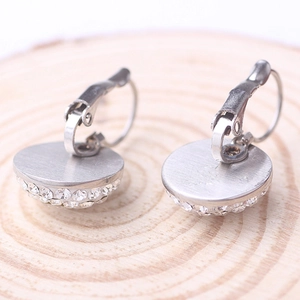 Macro shot of silver titanium steel hoop earrings with crystals on natural wood background