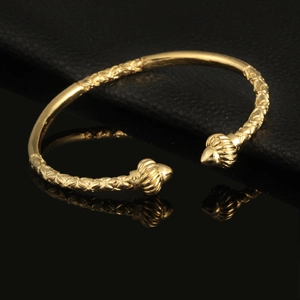 Macro shot of gold-plated open bangle with woven texture and spherical ends on leather
