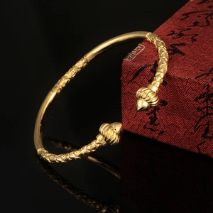 Detail of 18K gold-plated braided open bangle with threaded ball finials on black surface