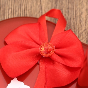 Close-up of a red satin ribbon bow with a faux gemstone on a heart-shaped gift box
