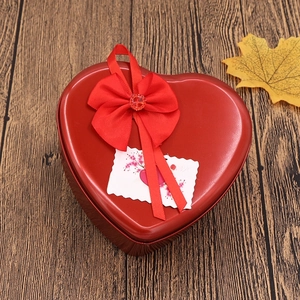Red heart-shaped tin gift box with satin bow and floral love card on vintage wood