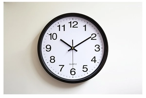 Detail of minimalist wall clock with black frame, bold Arabic numerals and quartz movement