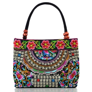 Ethnic style black canvas handbag with floral embroidery and wooden beads on white background