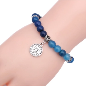 Dettaglio di bracciale con perline occhio di tigre blu e ciondolo a loto in argento al polso