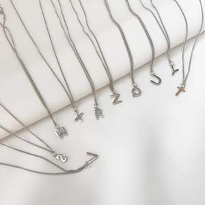 Row of 925 sterling silver necklaces featuring various letter pendants on white fabric