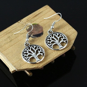 Vintage silver tree of life dangle earrings with circular hollow design on a wooden tray