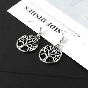 Detailed close-up of antique silver Tree of Life circular hollow drop earrings on a bicolour background