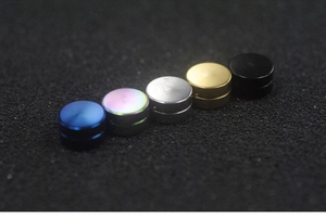 Macro shot of magnetic stud earrings in five metallic colors on a dark textured surface