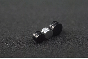 Macro shot of black and silver round magnetic stud earrings on a dark textured background