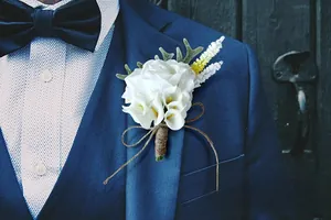 Close-up of white calla lily wedding corsage with rustic jute twine on a blue suit lapel