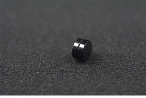 Macro shot of circular black magnetic earring with a matte finish on textured background
