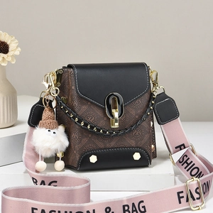 Retro monogram crossbody bag with pink woven strap and charm on a white display stand