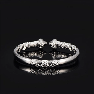 Detailed close-up of a silver open cuff bracelet featuring floral relief and swirl patterns