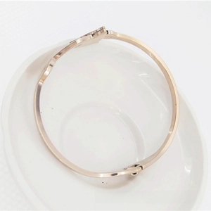 Detail of rose gold bangle with heart-shaped charm on a white ceramic plate