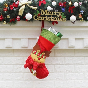 Festive red and green knitted Christmas stocking with reindeer design on a fireplace