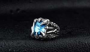 Macro shot of vintage steel ring with square blue gemstone on black leather and water drops