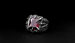 Macro detail of gothic dragon claw ring featuring a square red gemstone in silver finish