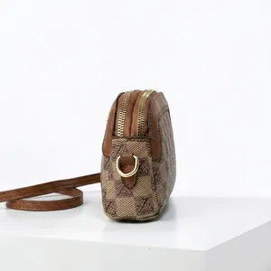 Detail of a brown monogram crossbody bag with double gold zippers and leather trim