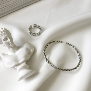 Artistic shot of silver twisted rope cuff bracelet and adjustable ring on white silk