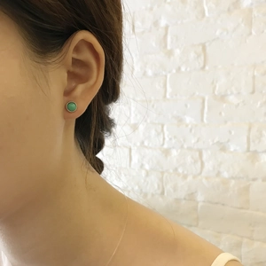Close-up of minimalist turquoise stud earrings with gold beaded edges on a female ear