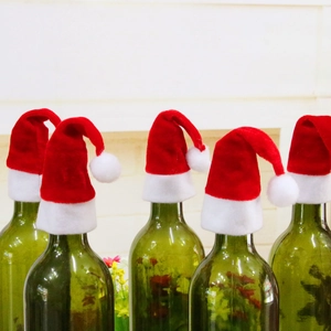 Fünf rote Plüsch-Weihnachtsmützen für Flaschen auf grünen Glasflaschen in Festdeko