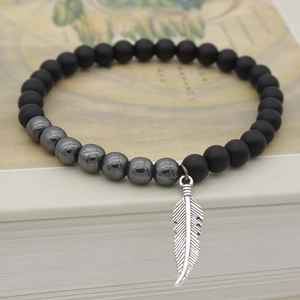 Matte black beaded bracelet with hematite accents and silver leaf pendant on a vintage book