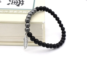Detail of matte black beads and hematite stones with a silver feather charm on a bracelet
