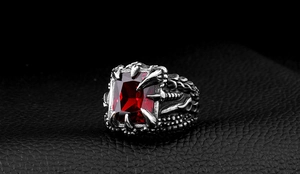 Gothic dragon claw ring detail with red zircon stone on black leather background