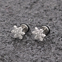 Detailed macro view of snowflake barbell earrings with crystals on a textured gray stone surface