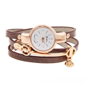 Detail of rose gold wrap-around watch with dark patterned strap and metal charms