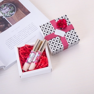 Close-up of pink shredded raffia paper filling a gift box with two lip balms and a bow