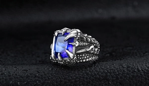 Detailed view of punk dragon claw ring with large blue zircon on a wet textured surface